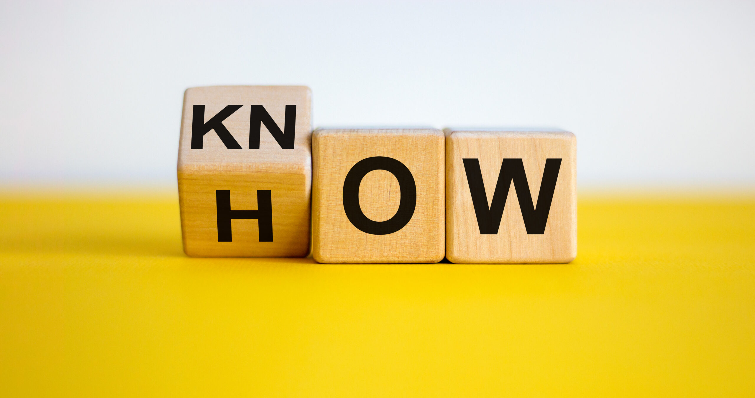 Know how and business concept. Turned cube and changed the word 'how' to 'know'. Beautiful yellow table, white background.