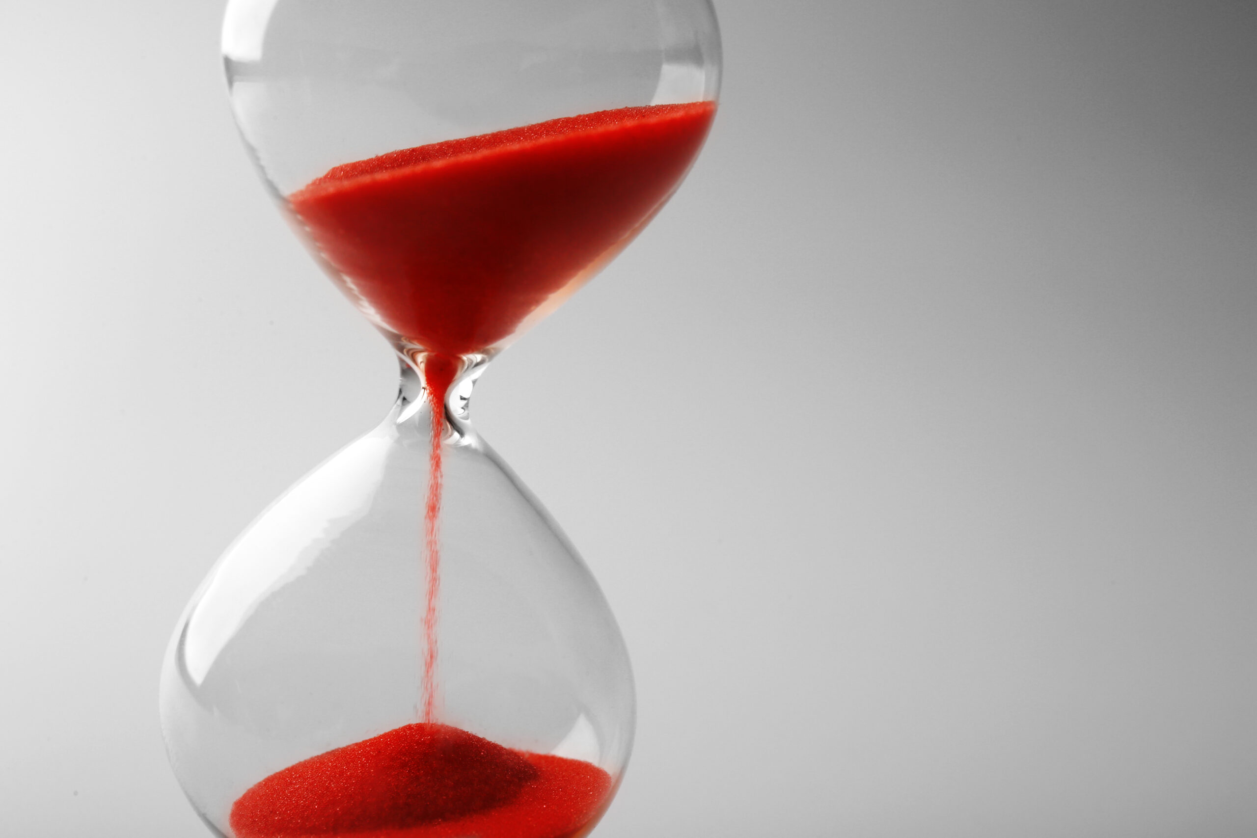 Hourglass with red sand falling on grey background
