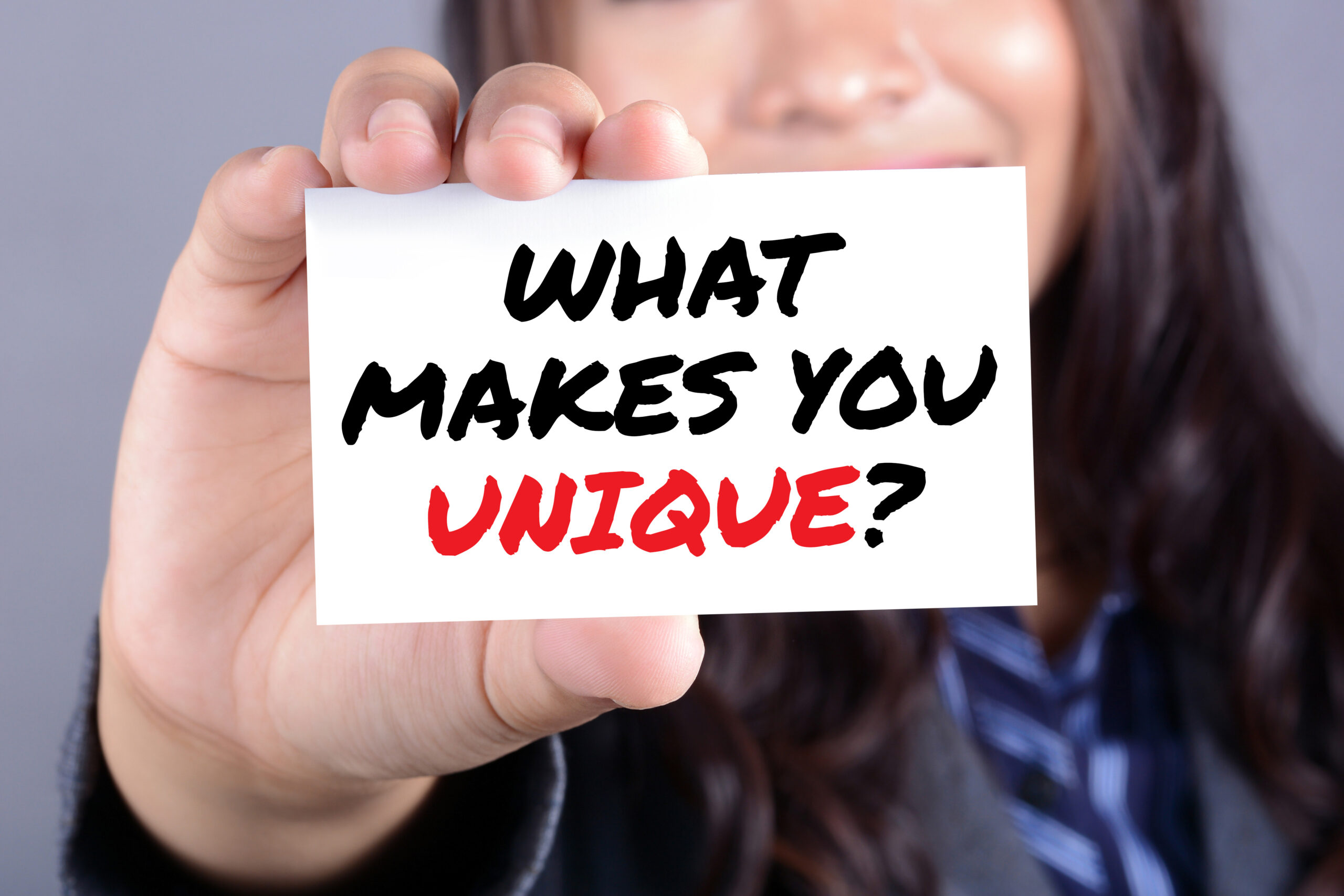 "WHAT MAKES YOU UNIQUE?", message on the card shown by a businesswoman
