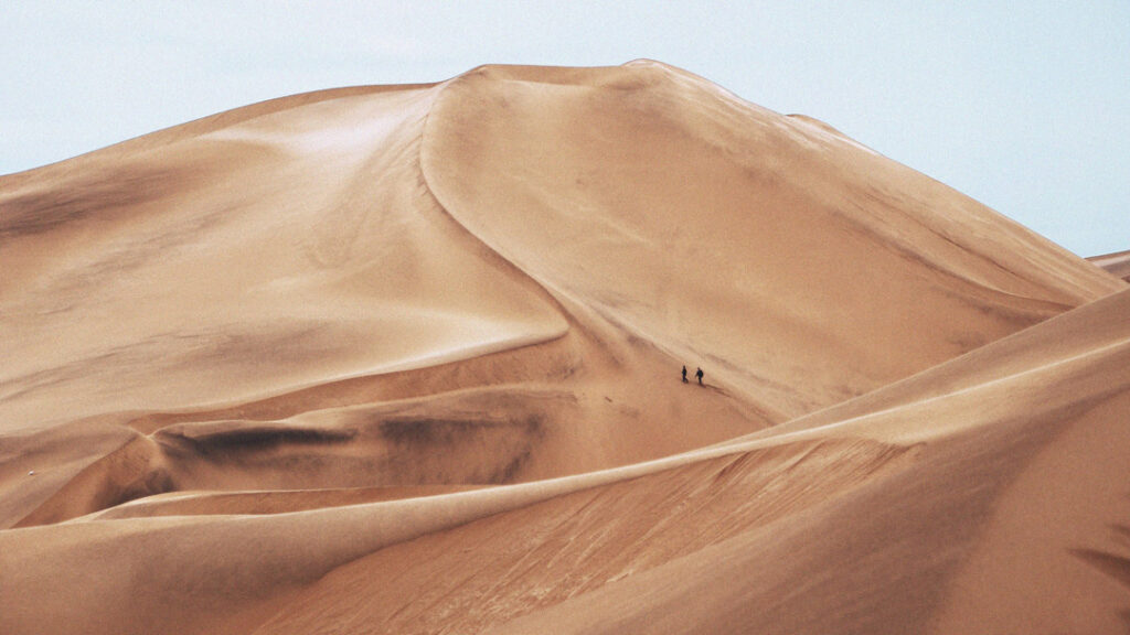 Sand dune with 2 small figures in black climbing